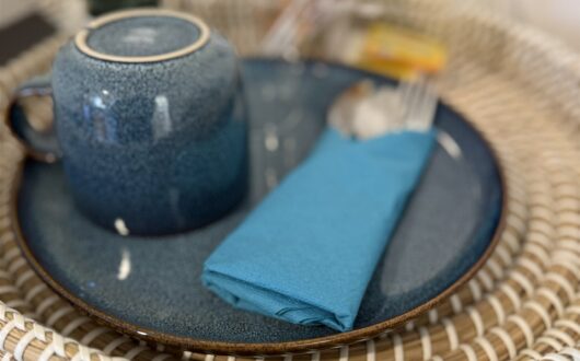 Blue crockery, cutlery and a napkin set out on a woven tray in teachers suite