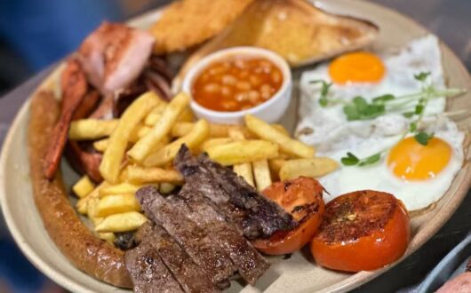 Big breakfast plate with steak, sausage, bacon, eggs, chips, beans, tomato and toast